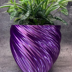 May include: A vibrant purple, spiral-patterned planter pot holding a green plant with white-speckled leaves. The pot has a glossy finish and a unique, textured design, adding a modern touch to home decor.