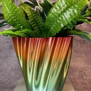 Puede incluir: Una maceta de color verde y naranja degradado con una superficie ondulada y texturizada. La maceta está llena de plantas verdes de hoja.