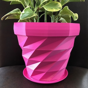 May include: A pink geometric planter with a plant with green and yellow leaves. The planter has a textured, diamond-shaped design.