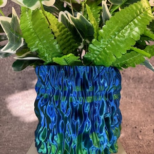 May include: A blue and green planter with a wavy, textured surface. The planter is filled with green leafy plants.