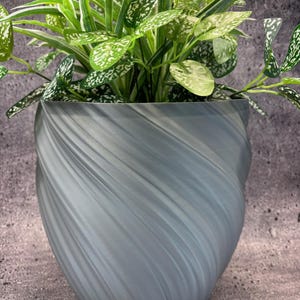 May include: A gray, swirled-design planter pot filled with a green plant with white speckled leaves. The pot has a smooth, textured surface and a unique, modern shape. The plant's leaves are a vibrant green, contrasting with the pot's muted gray color.