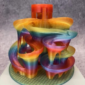 Op de afbeelding: Een regenboogkleurig 3D-geprint beeldhouwwerk met een torenvormige structuur en een basis met een rasterpatroon.
