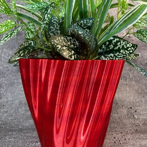May include: A red, wavy, textured ceramic planter with a green plant with white speckles growing inside.