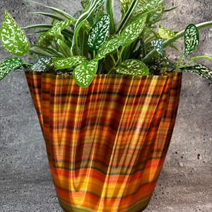 May include: A decorative plant pot with a unique, swirling design in shades of orange, yellow, and brown. The pot holds a vibrant green plant with white-speckled leaves, adding a touch of nature to any space. The pot's dimensions are approximately 8 inches in height and 9 inches in diameter.