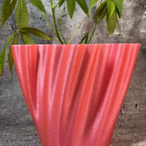 May include: A pink, wavy, 3D printed planter with a green plant growing out of it.