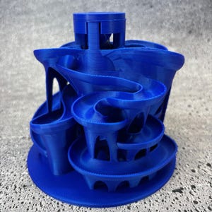 May include: A vibrant blue marble run toy with multiple spiraling tracks and architectural supports. The toy features a circular base and a tower at the top, designed for marbles to travel through the winding pathways. A fun and engaging toy for all ages.
