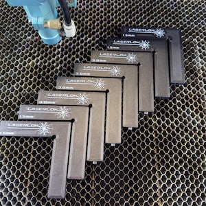 May include: A set of grey L-shaped LaserLok tools, each marked with measurements in millimetres. The tools are arranged in a stepped pattern, with the LaserLok logo and measurement details clearly visible. The background features a honeycomb pattern.