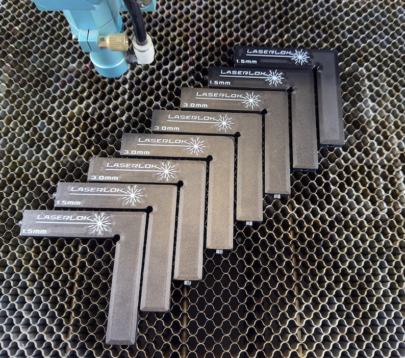 May include: A set of grey L-shaped LaserLok tools, each marked with measurements in millimetres. The tools are arranged in a stepped pattern, with the LaserLok logo and measurement details clearly visible. The background features a honeycomb pattern.