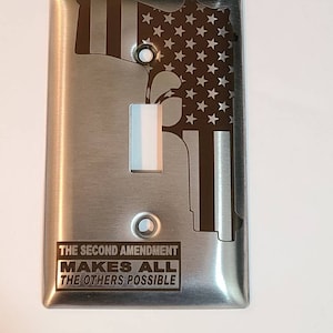 May include: A brushed stainless steel light switch cover with an American flag design and the text "The Second Amendment Makes All The Others Possible".