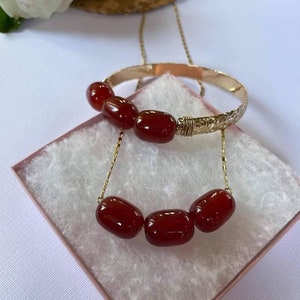 May include: A gold chain necklace and bracelet with red carnelian beads. The necklace has four beads and the bracelet has three beads.