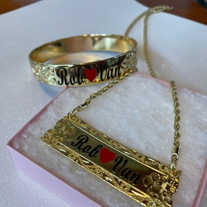 May include: Gold necklace and bracelet set with a heart and the names "Rob" and "Van" engraved on each piece.