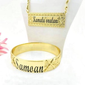 May include: A gold-coloured necklace inscribed with "Kamalu'onalani" and a matching bracelet inscribed with "Samoan." Both items feature detailed engraved patterns. The necklace is displayed on a white mannequin.