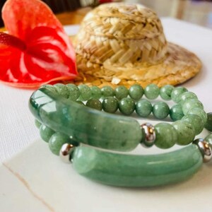 May include: Two green jade stone bracelets with silver accents. The bracelets are stacked on top of each other.