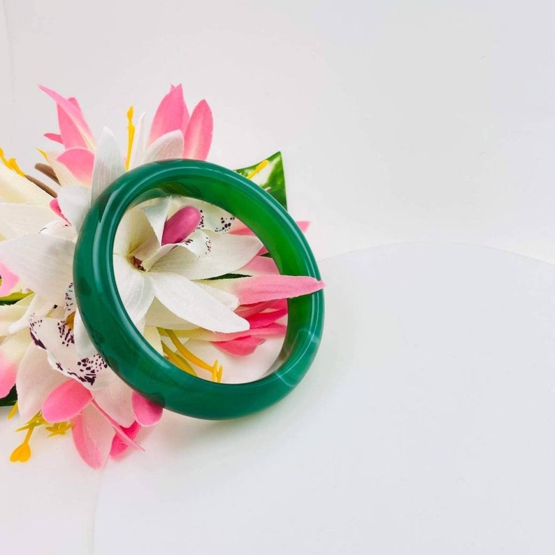 May include: A green jade bangle bracelet with white and pink flowers.