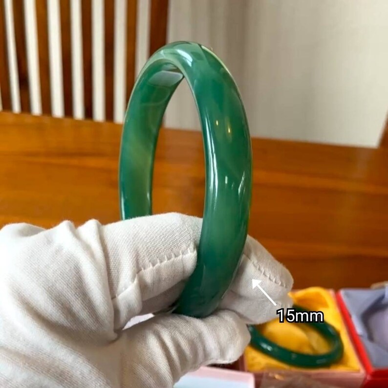 May include: A green jade bangle bracelet with a smooth, polished finish. The bracelet is 15mm wide.