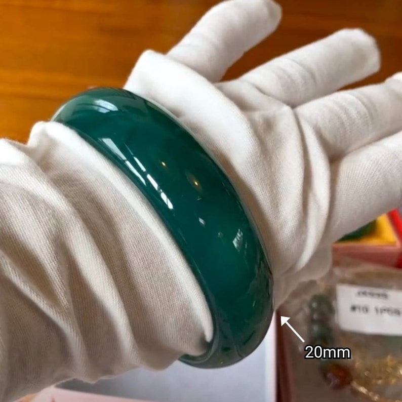 May include: A green jade bangle bracelet with a glossy finish. The bracelet is 20mm wide.