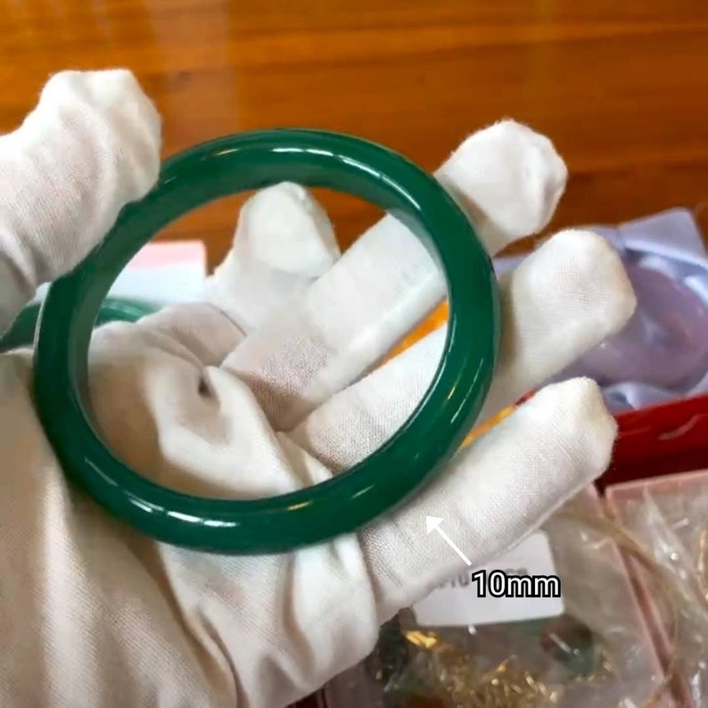 May include: A green jade bangle bracelet with a 10mm width. The bracelet is smooth and polished.