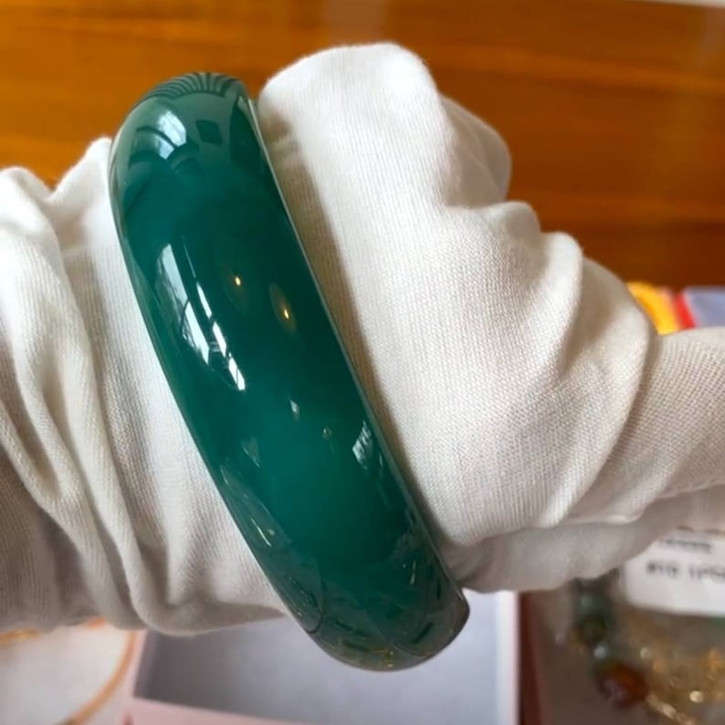 May include: A green jade bangle bracelet. The bracelet is smooth and polished.