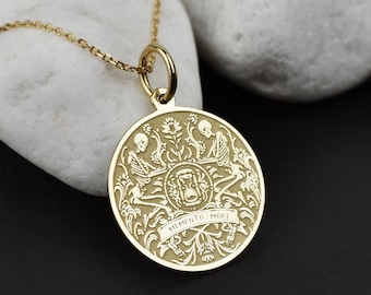 Könnte beinhalten: Goldfarbene Halskette mit Anhänger. Der runde Anhänger zeigt ein detailliertes Design mit floralen Elementen, Skeletten und dem Schriftzug "Memento Mori". Die Halskette wird auf einem weißen Stein präsentiert.