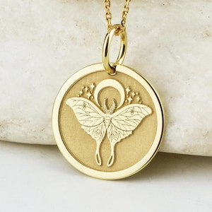 May include: Gold necklace with a round pendant featuring a detailed engraving of a moth with wings spread and a crescent moon above it.