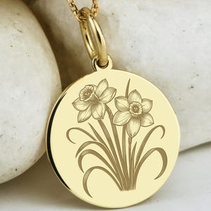 Könnte beinhalten: Goldfarbene Halskette mit rundem Anhänger mit eingraviertem Blumendesign von Narzissen. Die Kette hat kleine, runde Perlen. Der Anhänger hat einen Durchmesser von etwa 2,5 cm.