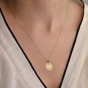 May include: A gold chain necklace with a small round pendant featuring a delicate angel wing design.
