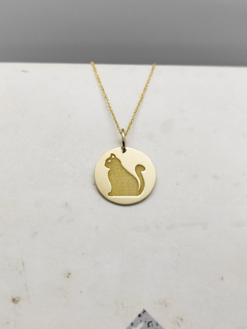 May include: A gold necklace with a round pendant featuring a cutout silhouette of a cat.