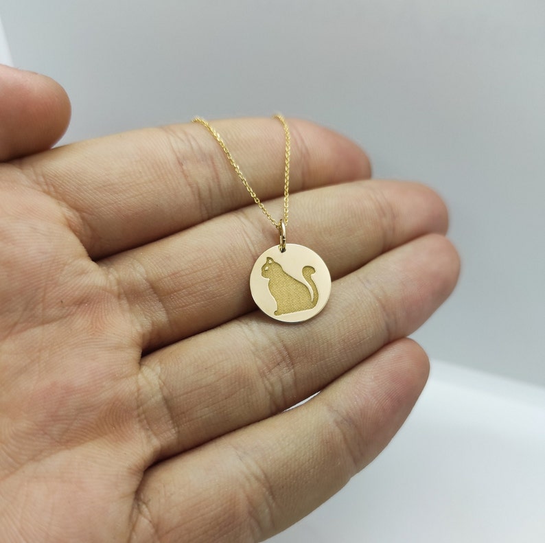 May include: A gold chain necklace with a round pendant featuring a cat silhouette.