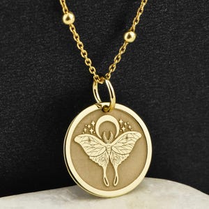 May include: Gold necklace with a round pendant featuring a detailed engraving of a moth with a crescent moon and stars.