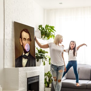 Pode incluir: Uma mulher e uma menina est&atilde;o em p&eacute; em frente a uma lareira com uma pintura de Abraham Lincoln na parede. A mulher est&aacute; segurando uma bolha rosa na frente do rosto de Lincoln. A menina est&aacute; em p&eacute; em um sof&aacute; com os bra&ccedil;os estendidos.