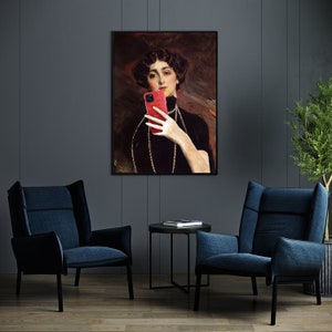 May include: A framed painting of a woman in a black dress holding a red smartphone in front of her face. The painting is set against a dark gray wall with two blue armchairs and a small black table in front of it.