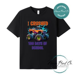 May include: A black short-sleeved t-shirt featuring a graphic of a colourful monster truck with large tyres. Above the truck, the orange text reads I CRUSHED, and below the truck, the purple text reads 100 DAYS OF SCHOOL. The design includes blue splashes.