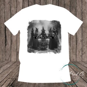 Witches in the forest design on custom t-shirt with the slogan “Girls Will Be Girls”. Feminist and empowering print on 100% cotton tee, perfect for girls and women, printed using high-quality DTF/DTG technology.