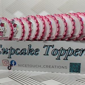 May include: A display of pink and white cupcake toppers with a scalloped edge. Each topper features a Hello Kitty design and a name. The box below reads "Cupcake Toppers" with social media icons and a QR code.