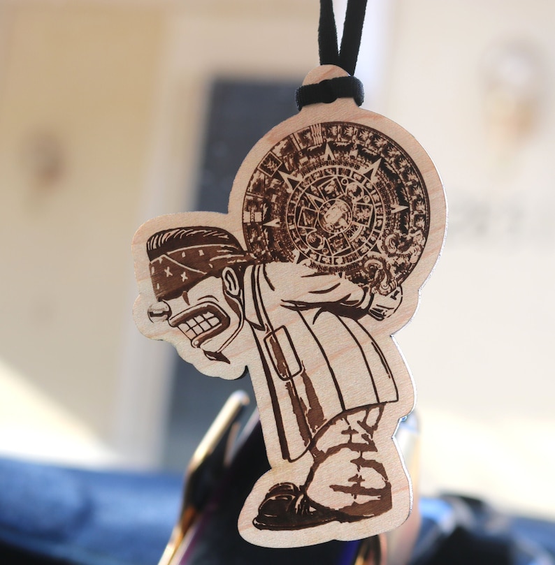May include: A wooden ornament featuring a cartoon character with a bandana carrying a circular design on their back. The design is intricate and detailed, resembling a sun or a clock face.