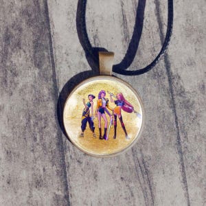 May include: Round pendant necklace with a cartoon illustration of three figures in colorful outfits. The pendant has a gold-colored frame and hangs from a black cord.