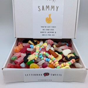 May include: A white box filled with a variety of colorful candies. The box lid has the name "SAMMY" and the message "YOU'VE GOT THIS! ALL OUR LOVE AUNTIE JASMINE & UNCLE PHIL XX". The box also has the text "LETTERBOX SWEETS" and the website address.