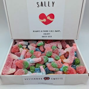 Peut inclure: Une boîte blanche remplie de bonbons gélifiés colorés assortis. Le couvercle de la boîte affiche le nom "SALLY", un cœur avec des bras et le texte "ALWAYS A PHONE CALL AWAY, ENJOY! DAISY XXX". La boîte est étiquetée "LETTERBOX SWEETS".