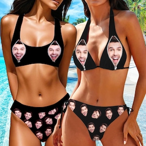 May include: Two black bikini tops with a zipper detail that reveals a face print. The bikini bottoms have a repeating face print.