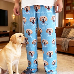 May include: Light blue pajama pants with a repeating pattern of a golden retriever's face and paw prints. The name "Charly" is printed below each dog face. The pants are worn with a white t-shirt and dark blue sandals.