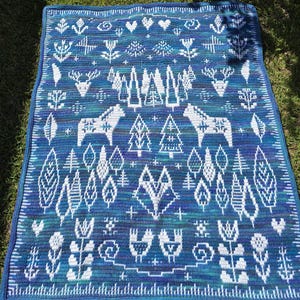 May include: A blue and white crocheted blanket with a Scandinavian folk art design featuring trees, deer, and flowers.