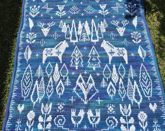 Könnte beinhalten: Eine blaue und weiße gehäkelte Decke mit einem skandinavischen Volkskunstdesign mit Bäumen, Hirschen und Blumen.