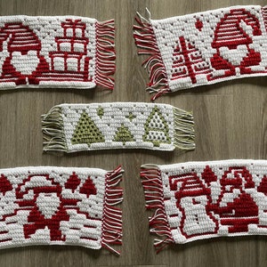 Pu&ograve; includere: Cinque tovagliette natalizie all'uncinetto fatte a mano. Ogni tovaglietta bianca presenta un diverso design festivo rosso e bianco, tra cui Babbo Natale, alberi di Natale e regali. I bordi sono rifiniti con frange rosse e bianche.