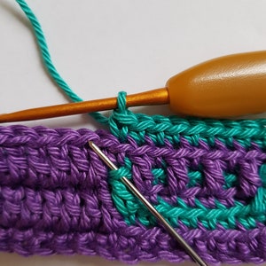 May include: A close-up of a crochet project with a purple and teal yarn. A crochet hook is being used to work a stitch in the teal yarn.