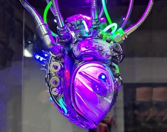 May include: A metallic, steampunk-style heart sculpture with intricate gears and tubing. It is illuminated with vibrant purple and green lights.