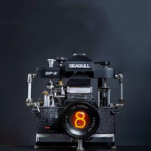 Puede incluir: Una cámara Seagull DF-2 negra con una pantalla digital roja que muestra el número 8. La cámara tiene un objetivo con el texto "f=58mm" y "1:2" impreso en él.