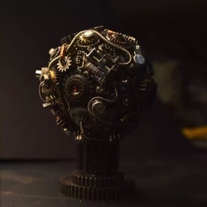 Pu&ograve; includere: Una scultura sferica realizzata con ingranaggi metallici, ruote dentate e altri componenti industriali. La scultura &egrave; montata su una base realizzata con materiali simili.
