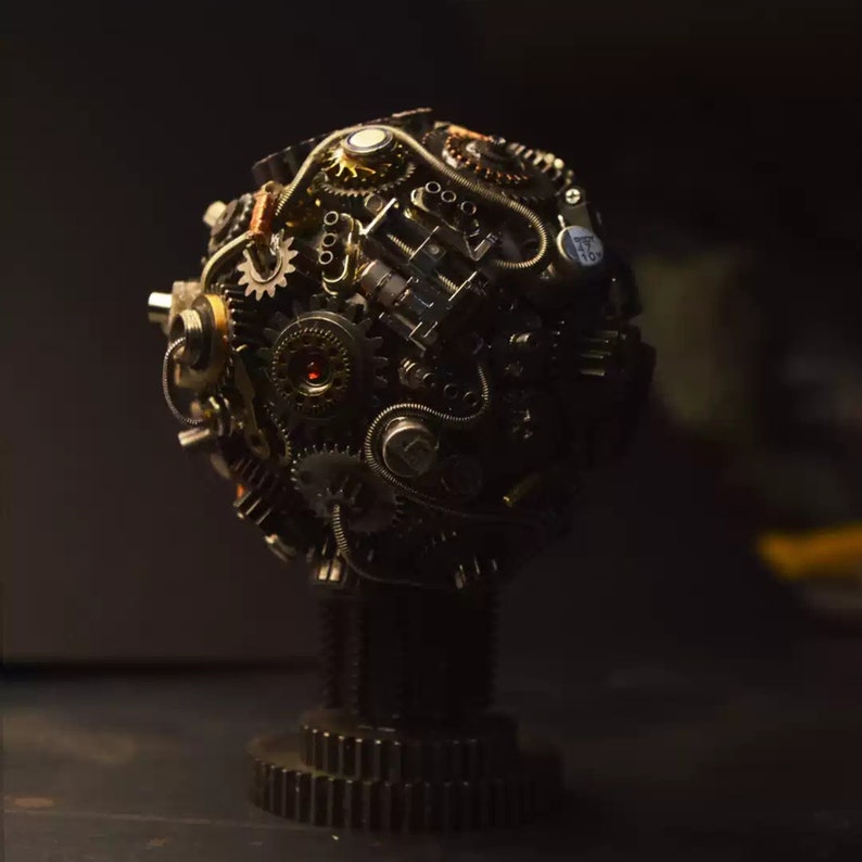 Pu&ograve; includere: Una scultura sferica realizzata con ingranaggi metallici, ruote dentate e altri componenti industriali. La scultura &egrave; montata su una base realizzata con materiali simili.