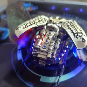 Puede incluir: Una escultura detallada de escarabajo mecánico, de color plateado, con luces LED rojas y azules. El escarabajo tiene engranajes intrincados y un diseño realista.