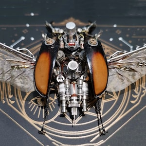 May include: A steampunk-style beetle sculpture crafted from metal and wood. The beetle features intricate details, including gears, pipes, and a small microphone. The beetle is positioned on a black surface with a gold design.